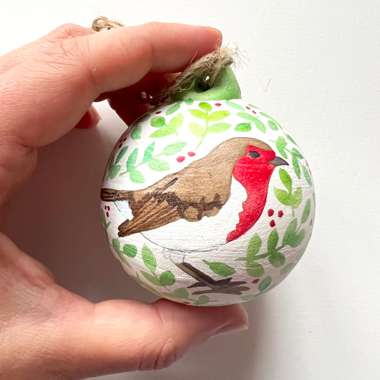 A collection of hand-painted ceramic Christmas baubles with various woodland animal designs including a fox, bear, deer, robin, rabbit, and squirrel, surrounded by green blue leaves and red berries.