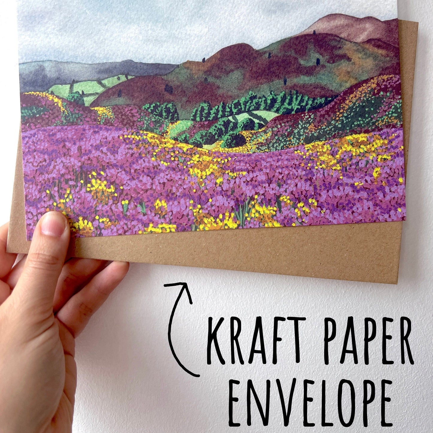 Rolling Hills Countryside Greetings Card with a Kraft paper envelope being held up by a hand with a white background. with text kraft paper envelope.