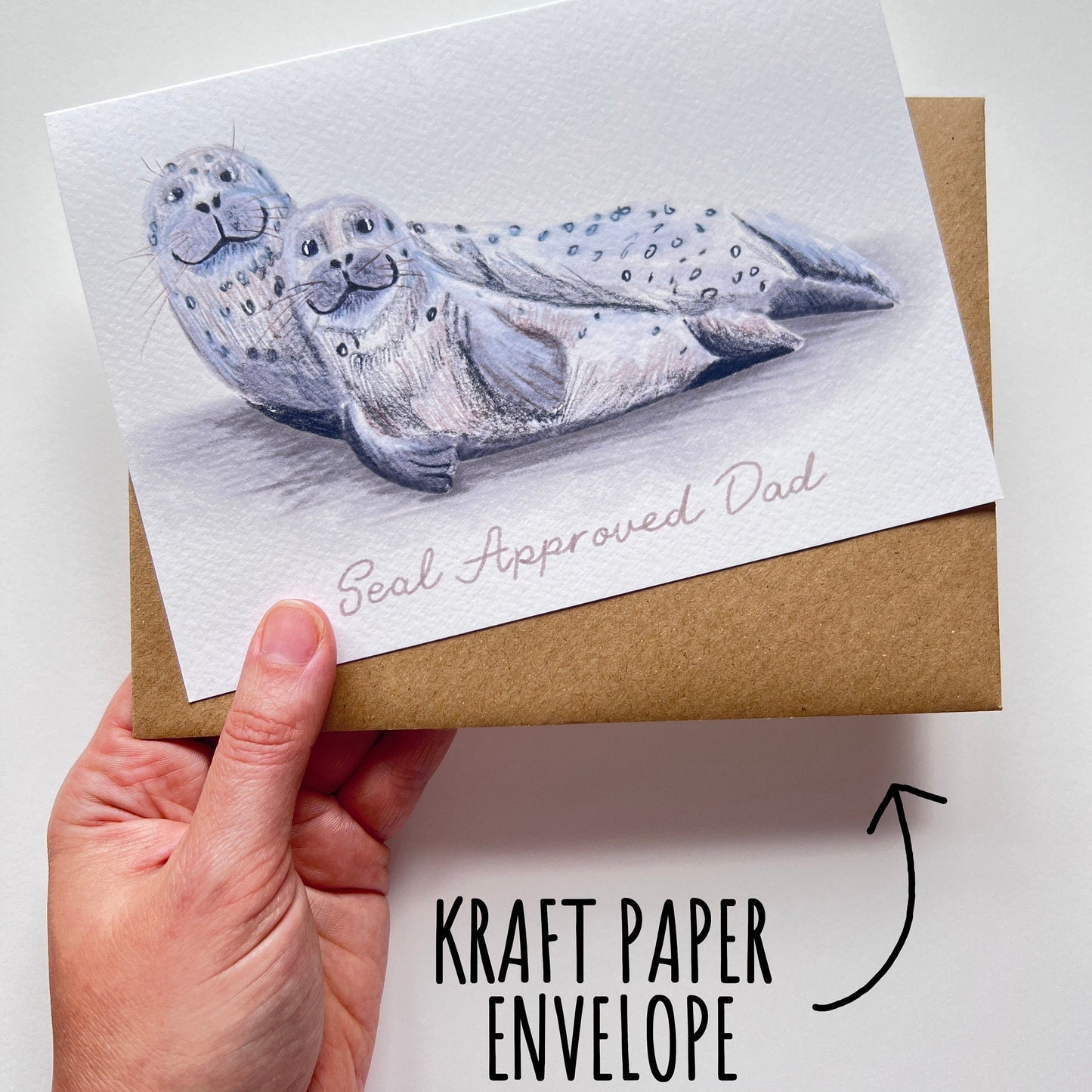 Seal Approved Dad Birthday Day Card being held up with its envelope against a white background. with the text kraft paper envelope.