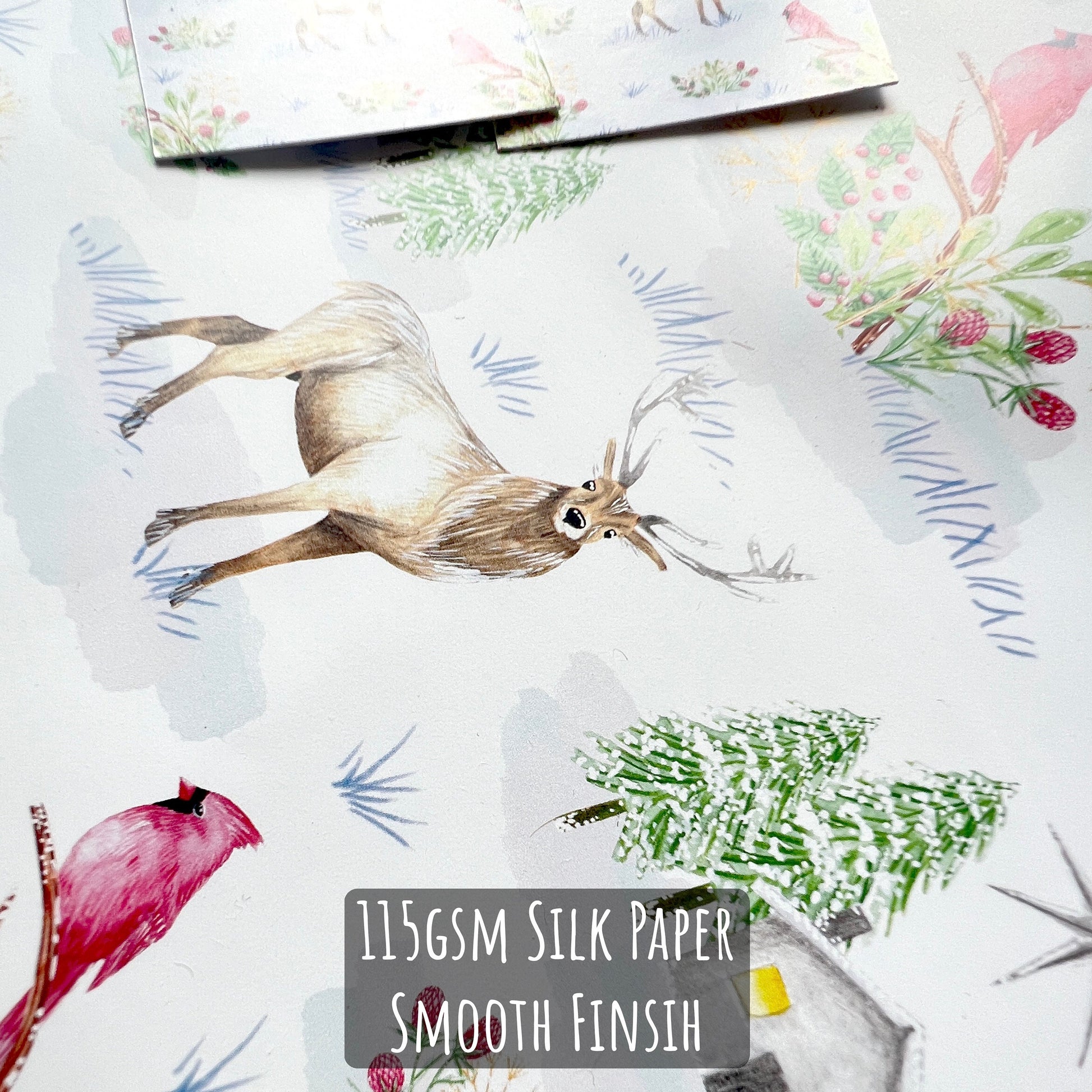 Snowy Winter Scene Wrapping Paper close up showing the details of the illustration and paper stock. with text 115gsm silk paper smooth finish.