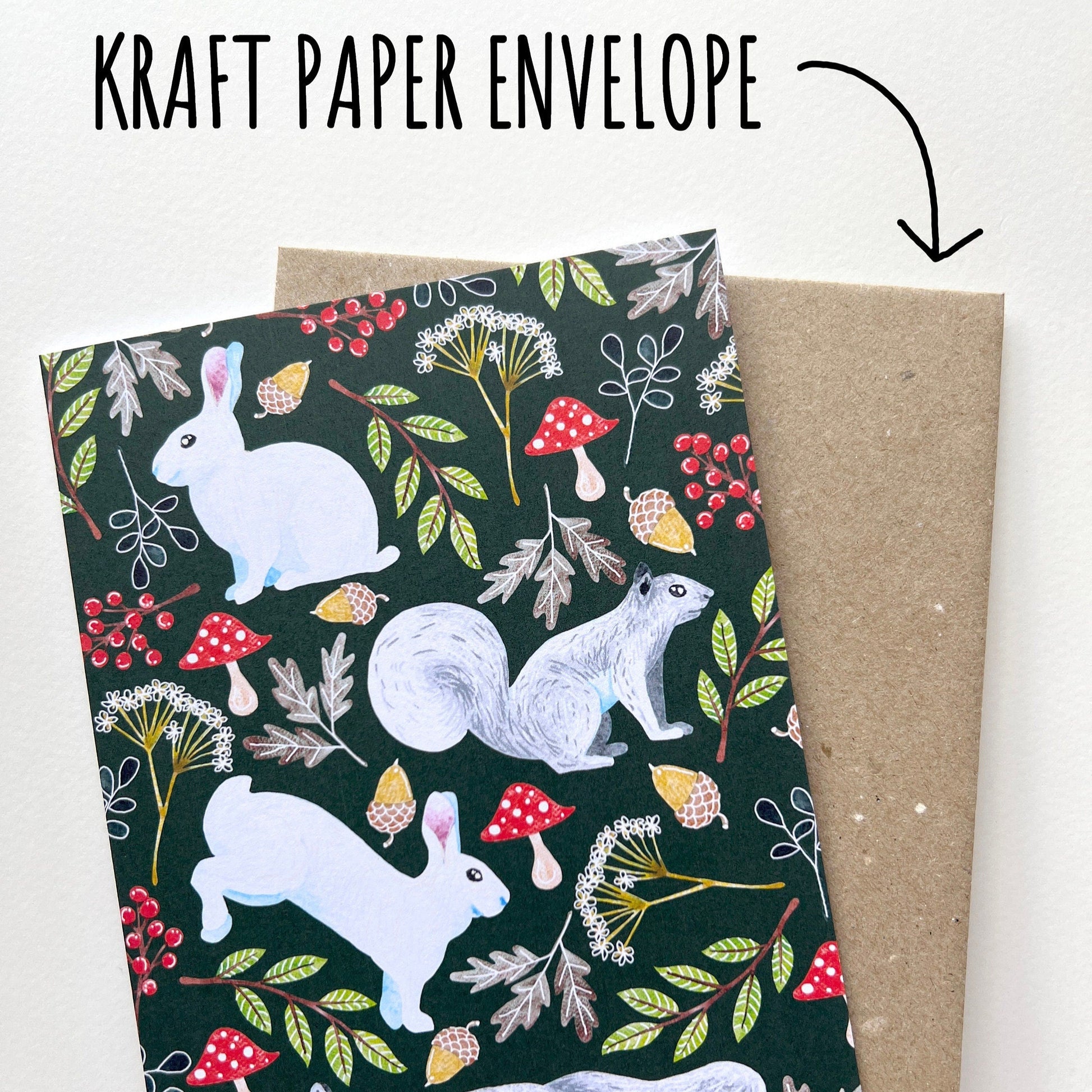 Kraft paper envelope with a forest-themed design featuring animals and plants, held by a hand.
