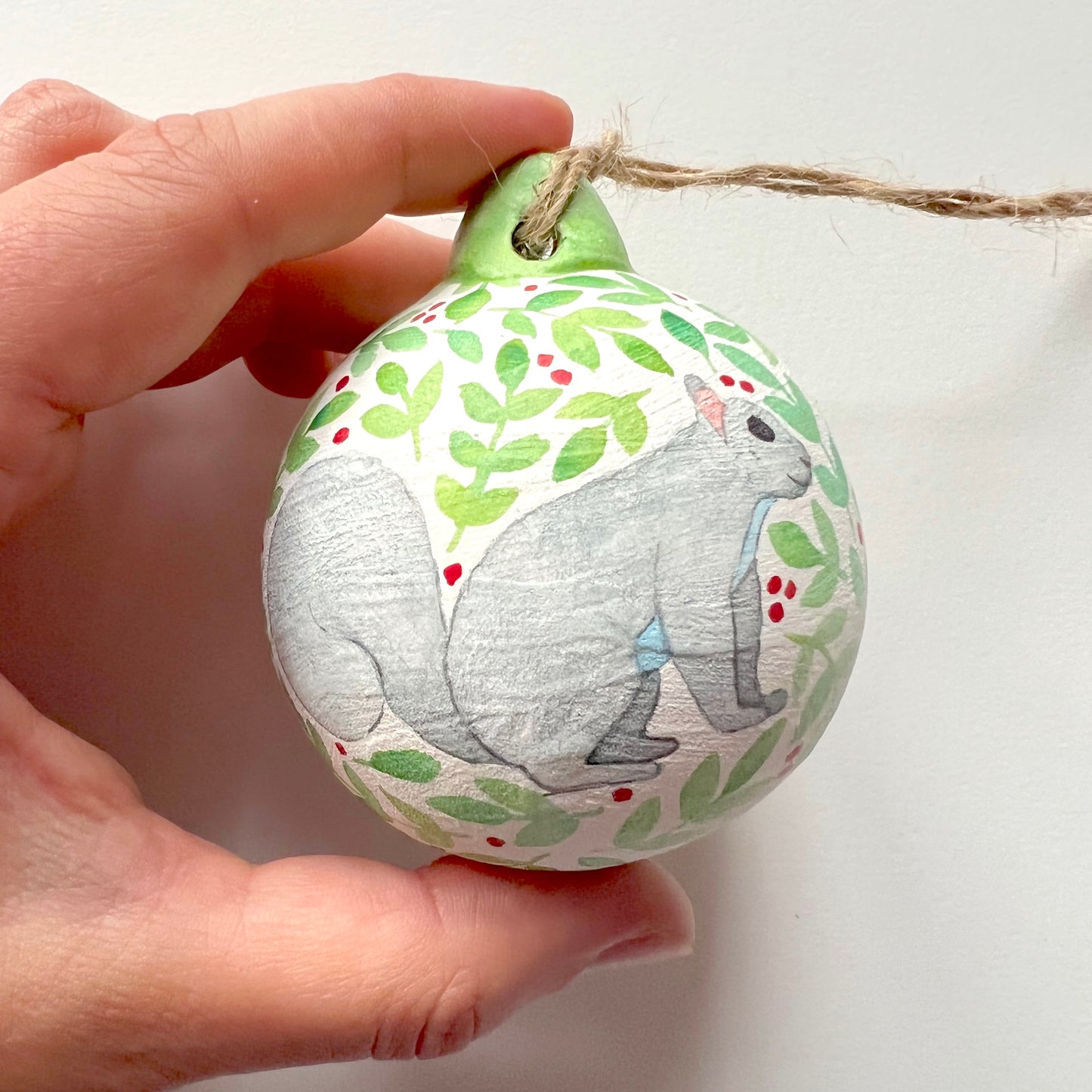 A collection of hand-painted ceramic Christmas baubles with various woodland animal designs including a fox, bear, deer, robin, rabbit, and squirrel, surrounded by green blue leaves and red berries.