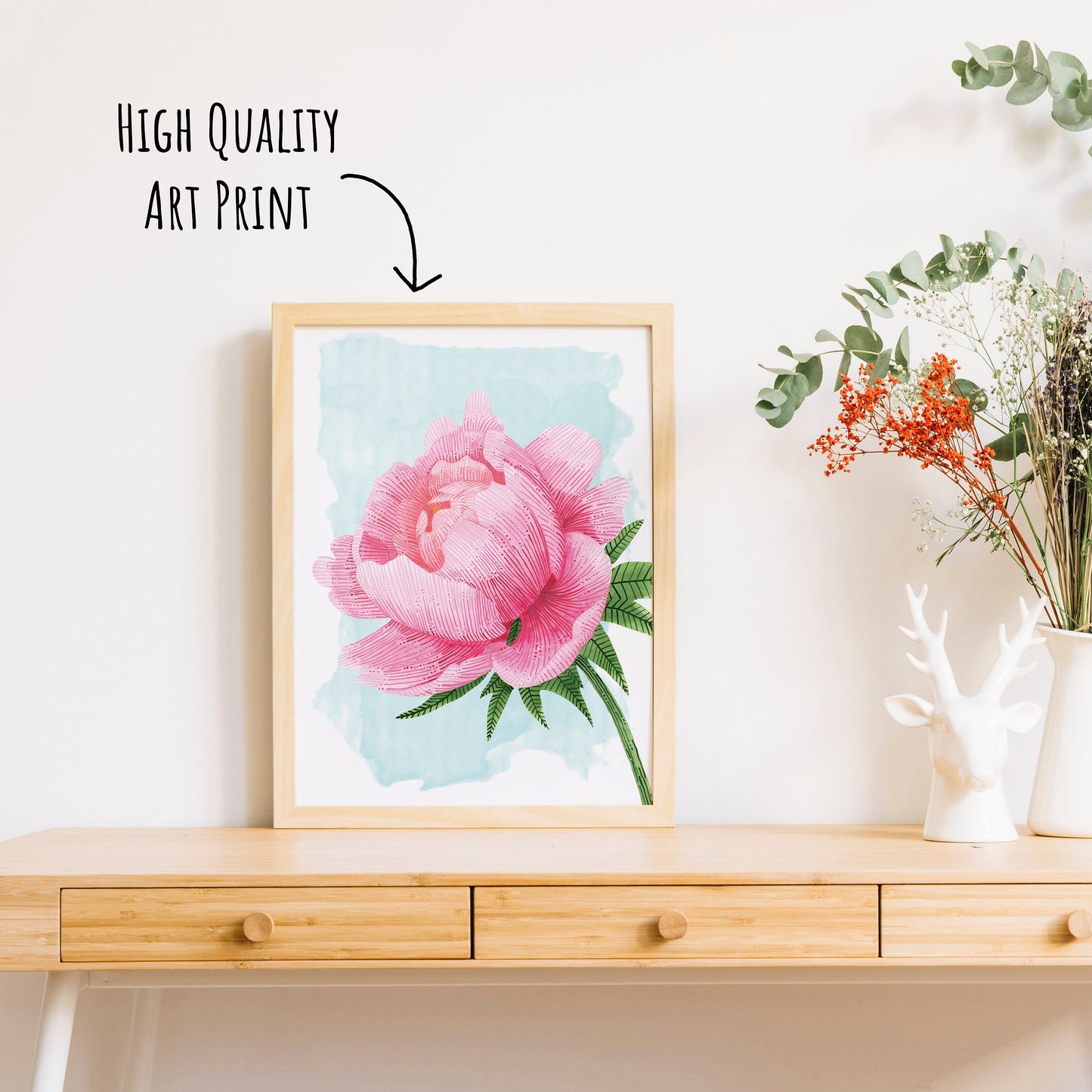 vibrant pink peony art print in a light wooden frame on a table top with a vase of dried foliage. (framed not included in purchase)