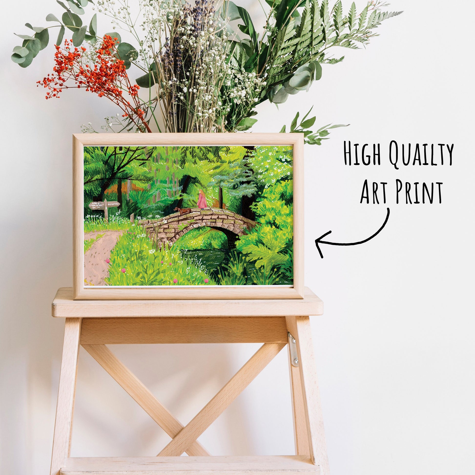 Vibrant Woodland Walk Art Print  in a light wooden frame on a coffee table with dried foliage behind with a white background.