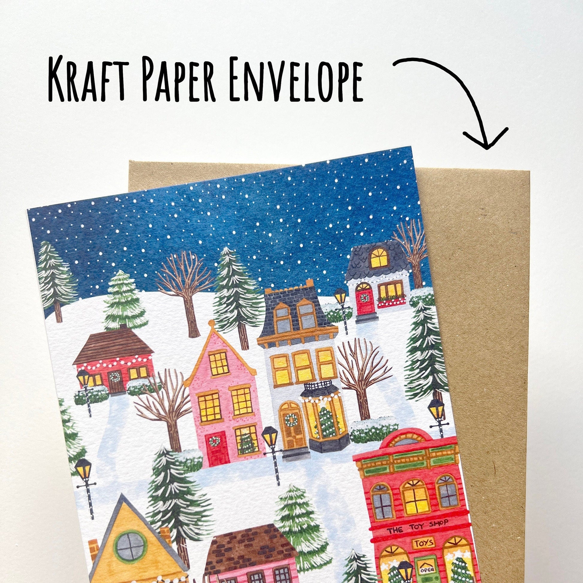Greeting card with winter village design held over a kraft paper envelope.