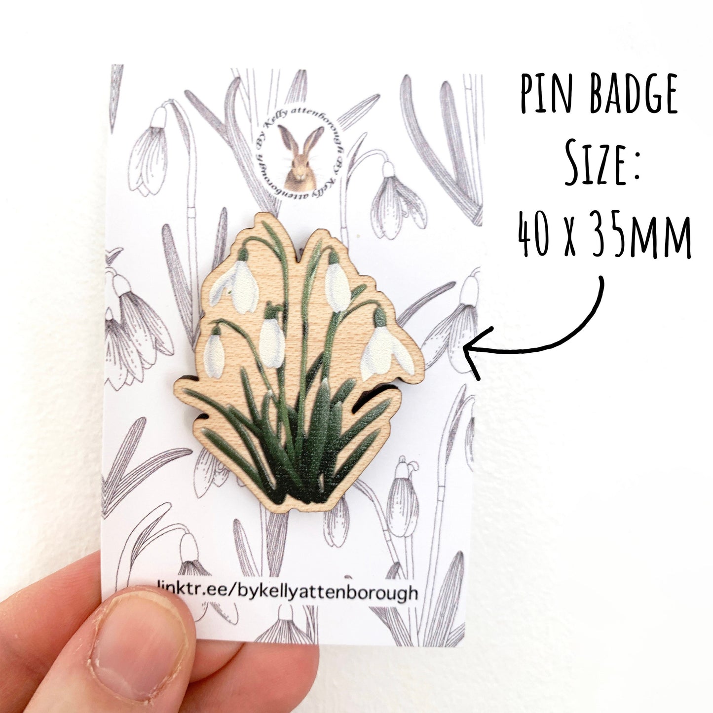 Wildflower Snowdrop Wooden Pin Badge on a backing card being held up on a white background. with the text pin badge size 40 x 35 mm.