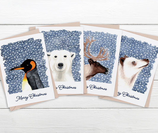 Set of four Christmas cards featuring animals (a penguin, a polar bear, a reindeer, and a white fox) on a white wooden surface.