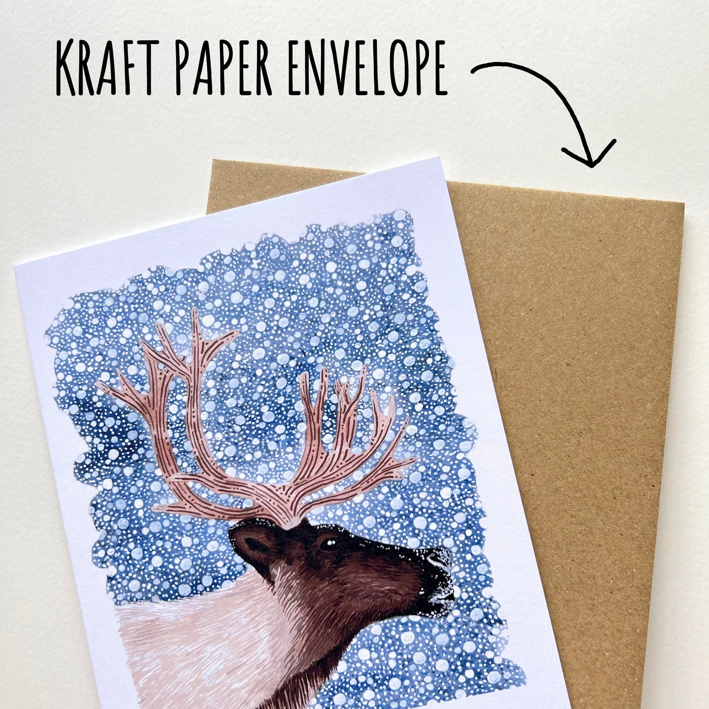 Kraft paper envelope with a Christmas card featuring a reindeer illustration on a white background.