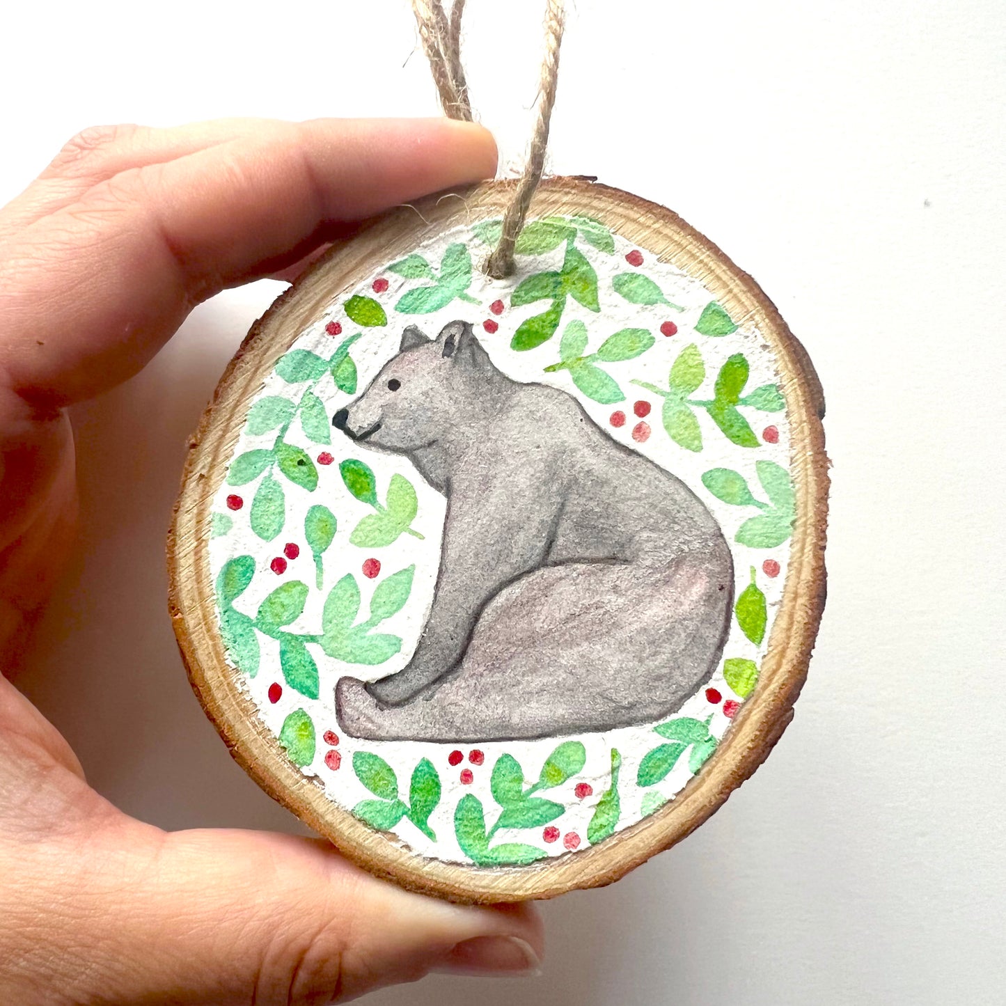 Hand-painted wooden slice Christmas decorations featuring various woodland animal designs including a fox, bear, deer, robin, rabbit, and squirrel, surrounded by green and red painted foliage.