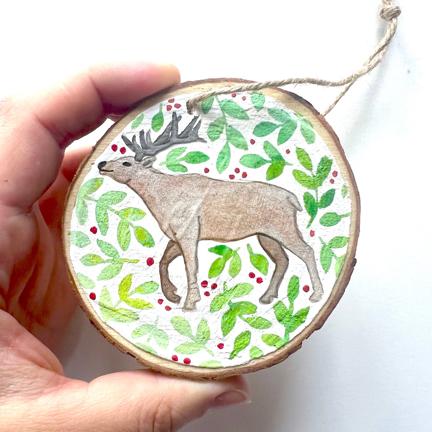 Hand-painted wooden slice Christmas decorations featuring various woodland animal designs including a fox, bear, deer, robin, rabbit, and squirrel, surrounded by green and red painted foliage.