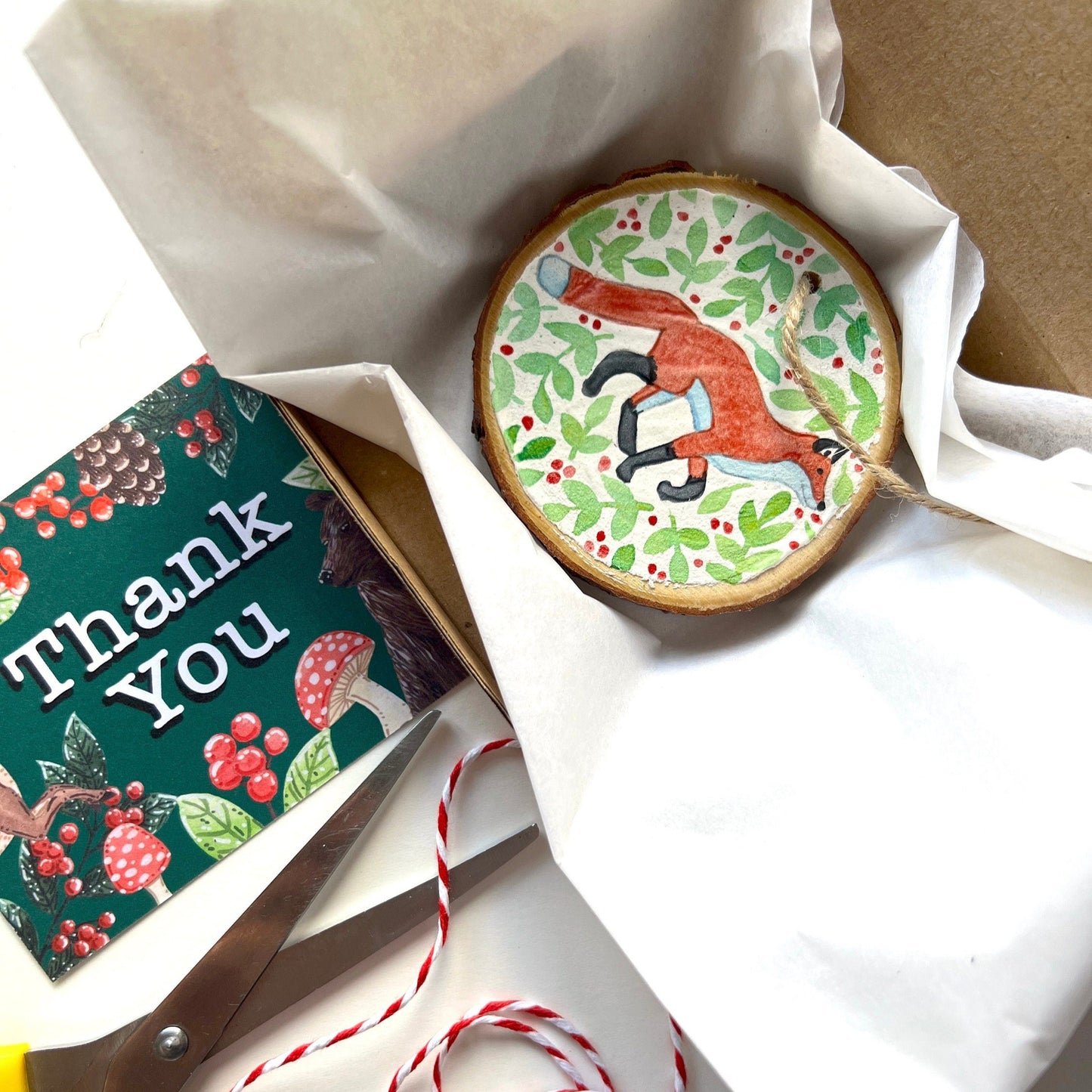 Decorative cookie with fox design, 'Thank You' card, scissors, and string on a white surface