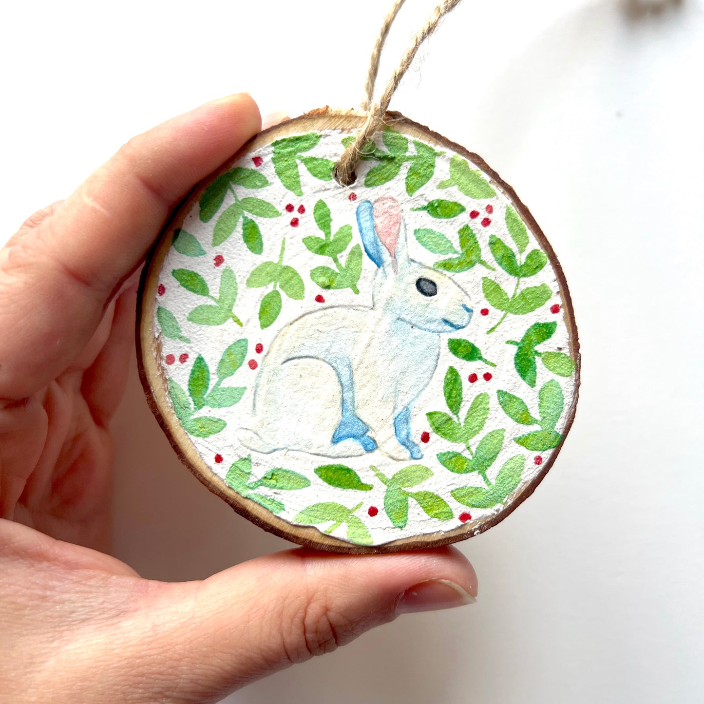 Hand-painted wooden slice Christmas decorations featuring various woodland animal designs including a fox, bear, deer, robin, rabbit, and squirrel, surrounded by green and red painted foliage.