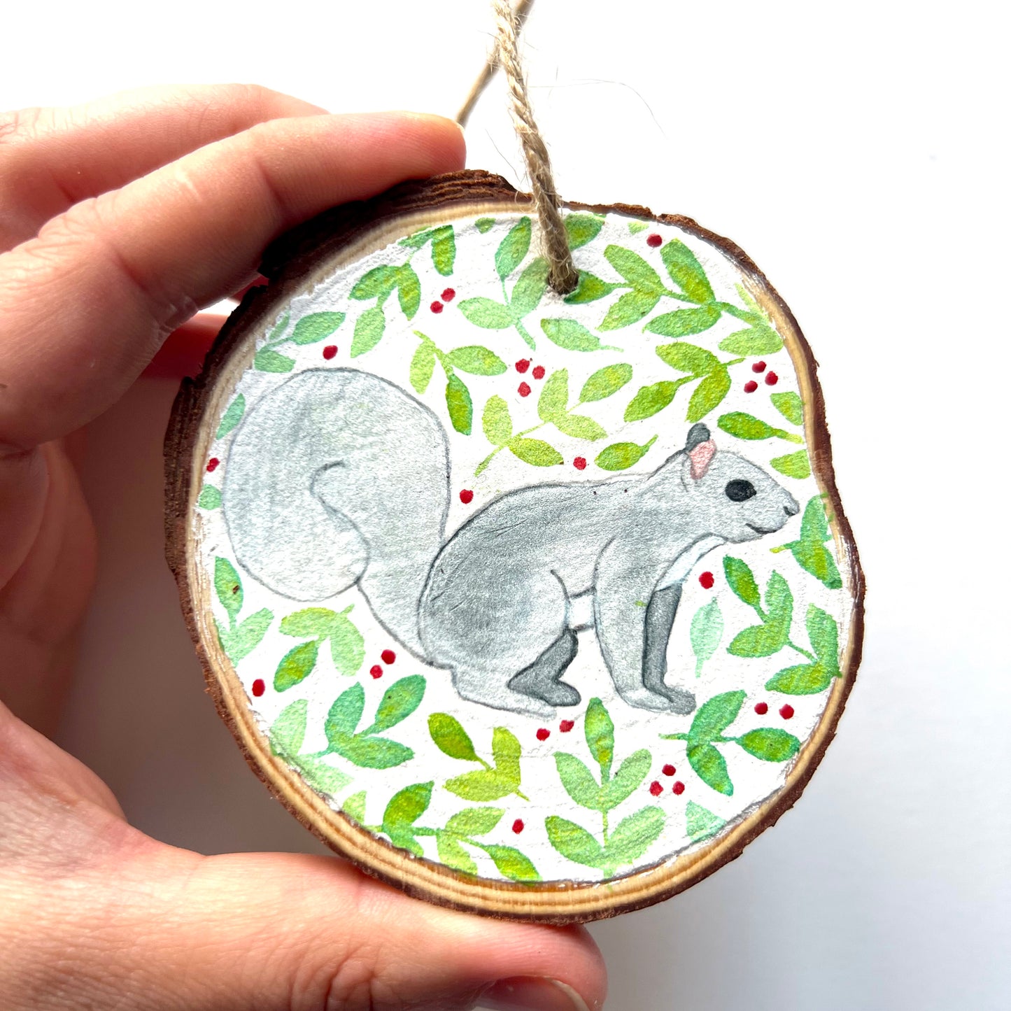 Hand-painted wooden slice Christmas decorations featuring various woodland animal designs including a fox, bear, deer, robin, rabbit, and squirrel, surrounded by green and red painted foliage.