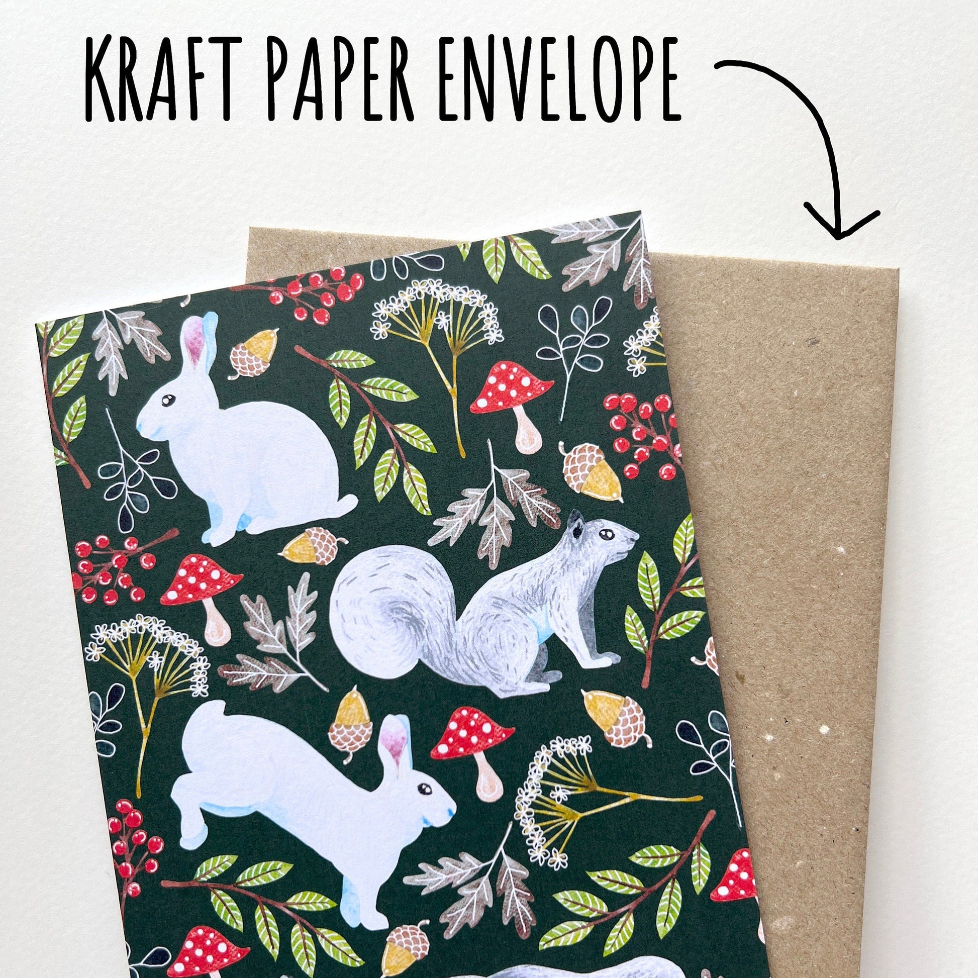 Kraft paper envelope with a forest-themed design featuring animals and plants, held by a hand. with a white background.