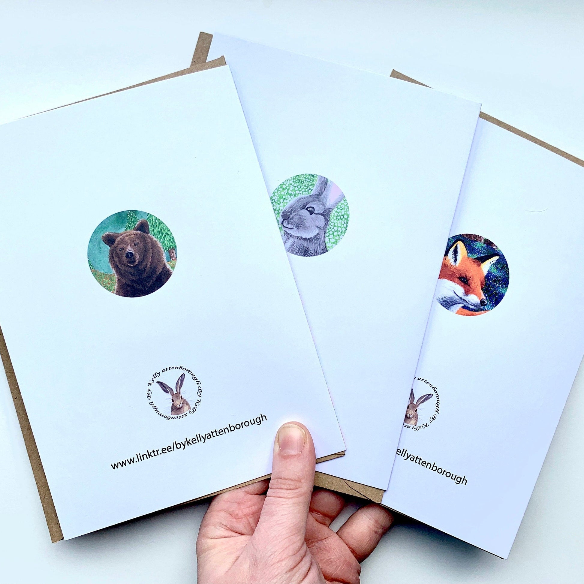 Three back of greeting cards with animal illustrations in circles held by a hand on a white background.
