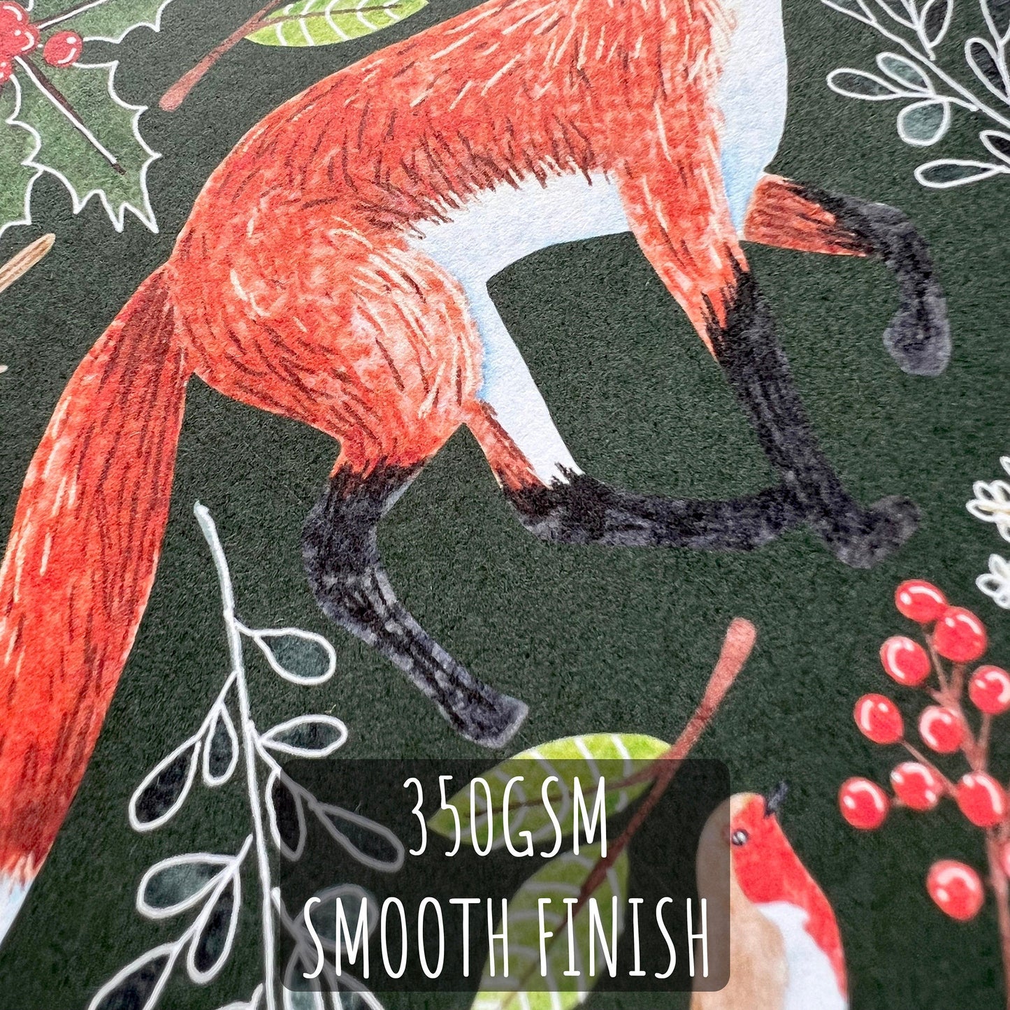 Card  close up showing a fox illustration and holly leaves on a dark background, featuring text '350GSM SMOOTH FINISH'.