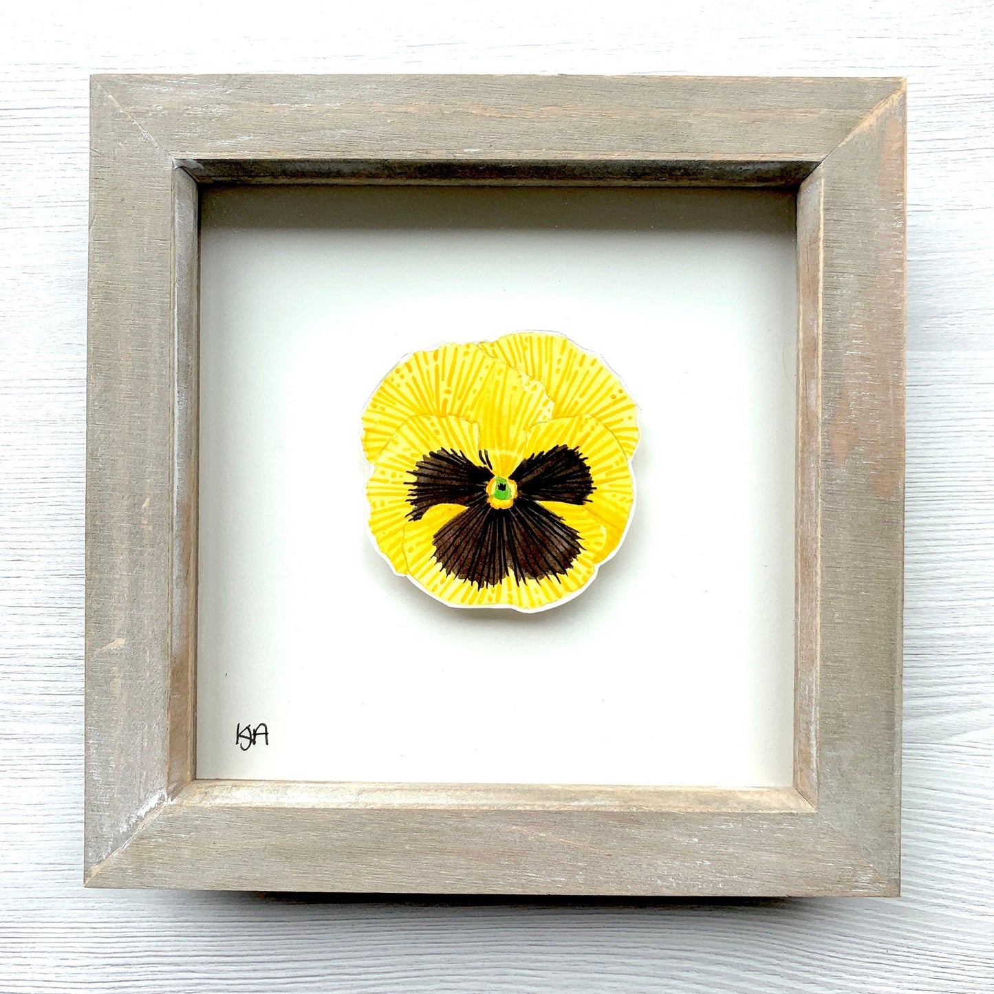 Hand painted vibrant yellow and black pansy flower on a piece of paper, with the artwork placed in a rustic washed effect wooden frame.