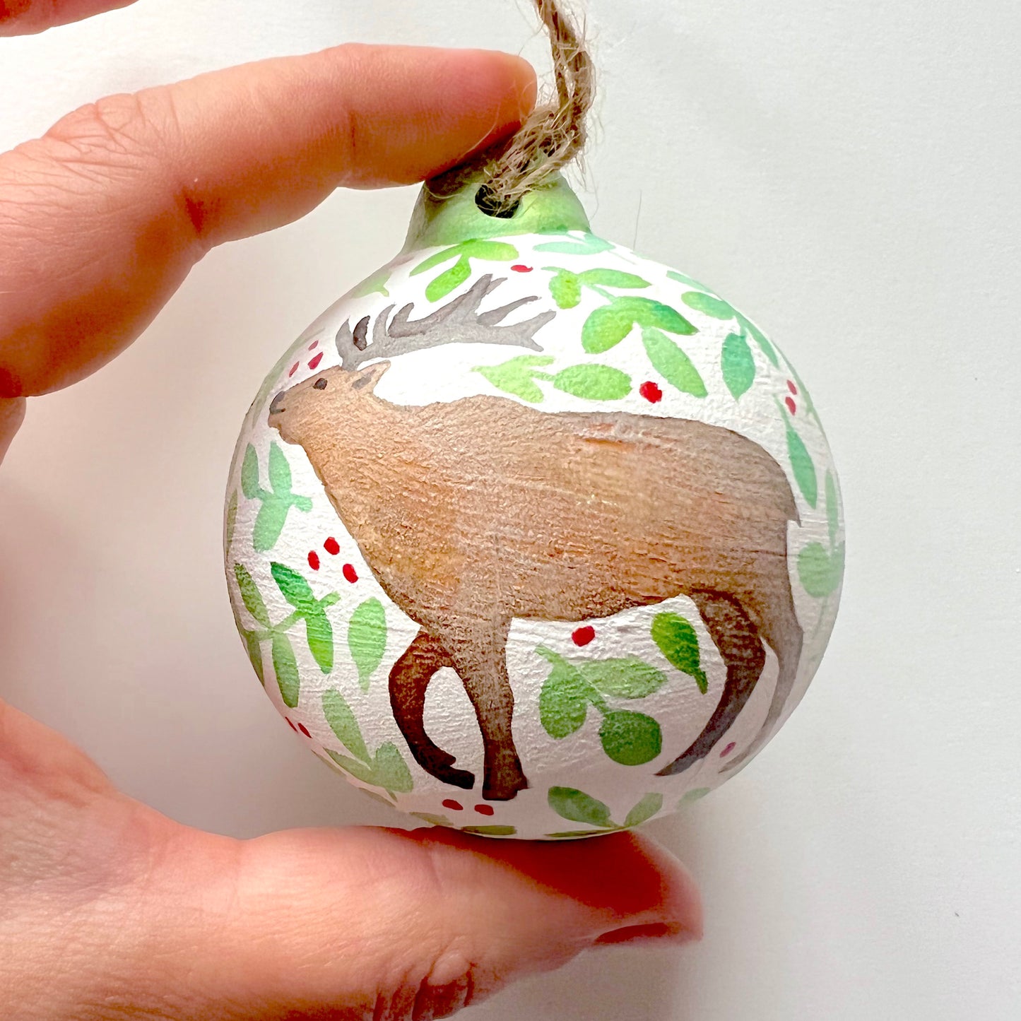 A collection of hand-painted ceramic Christmas baubles with various woodland animal designs including a fox, bear, deer, robin, rabbit, and squirrel, surrounded by green blue leaves and red berries.