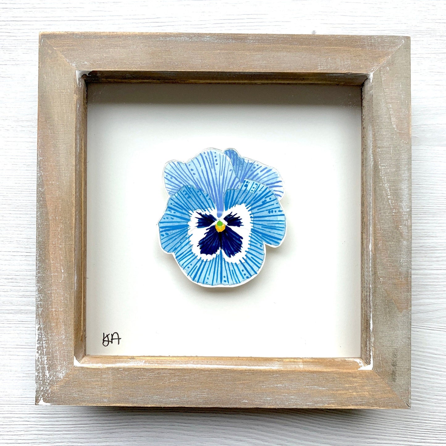 A hand-painted watercolor painting of a blue and white pansy flower, mounted in a rustic wooden frame.