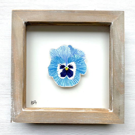 A hand-painted watercolor painting of a blue and white pansy flower, mounted in a rustic wooden frame.