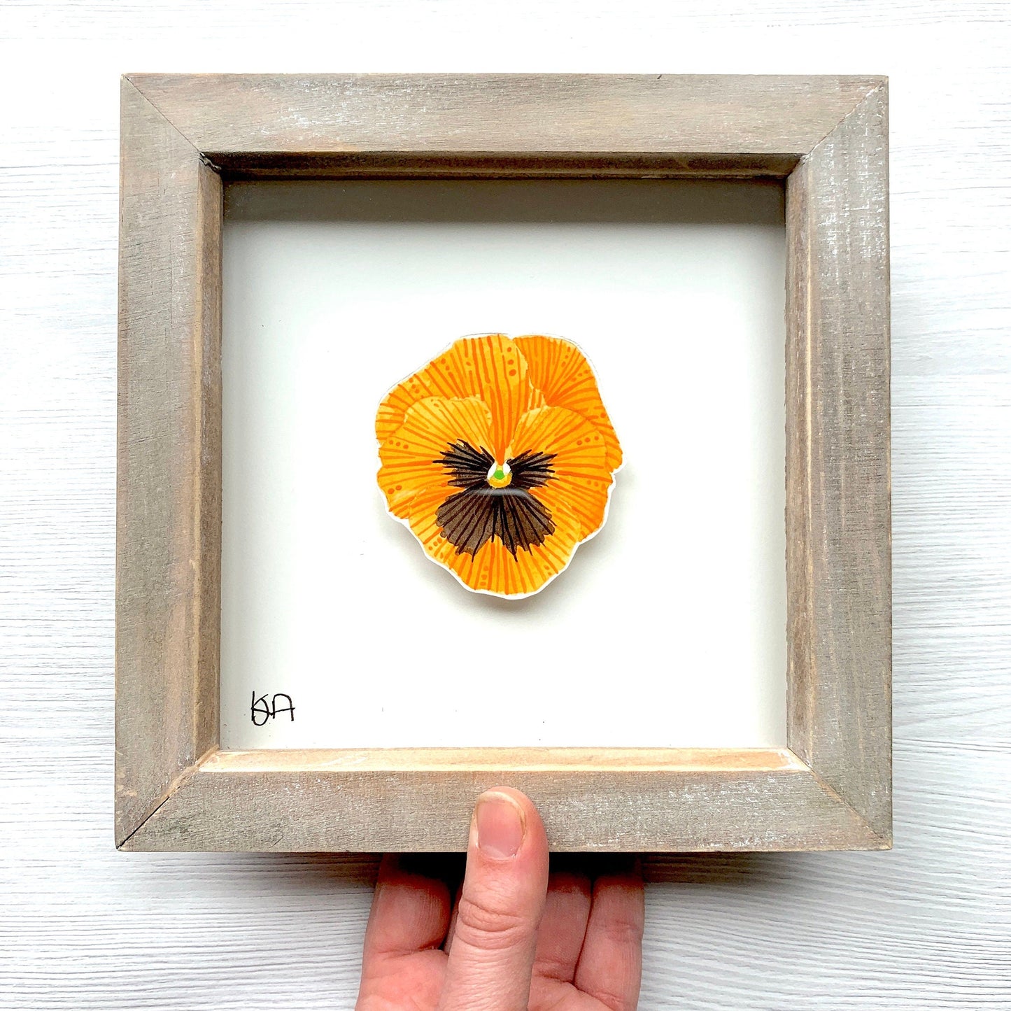 Framed orange flower painting with a hand holding it against a white background