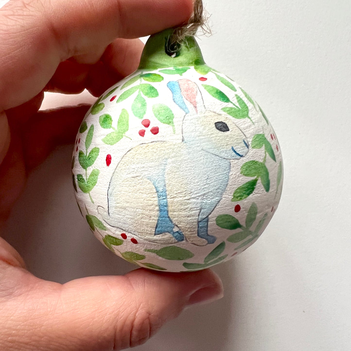 A collection of hand-painted ceramic Christmas baubles with various woodland animal designs including a fox, bear, deer, robin, rabbit, and squirrel, surrounded by green blue leaves and red berries.