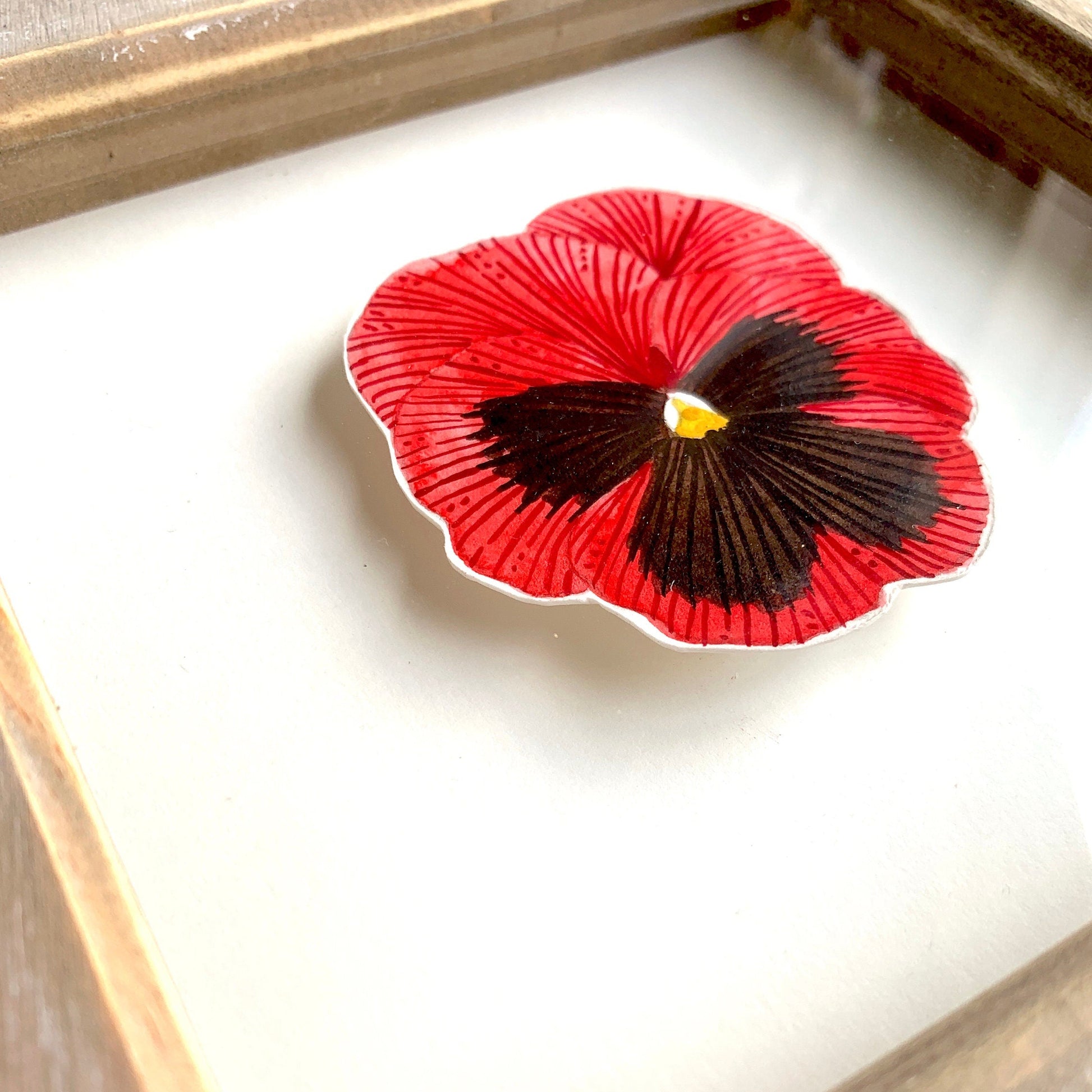 Red and black pansy flower-like design on a white background with a wooden frame.