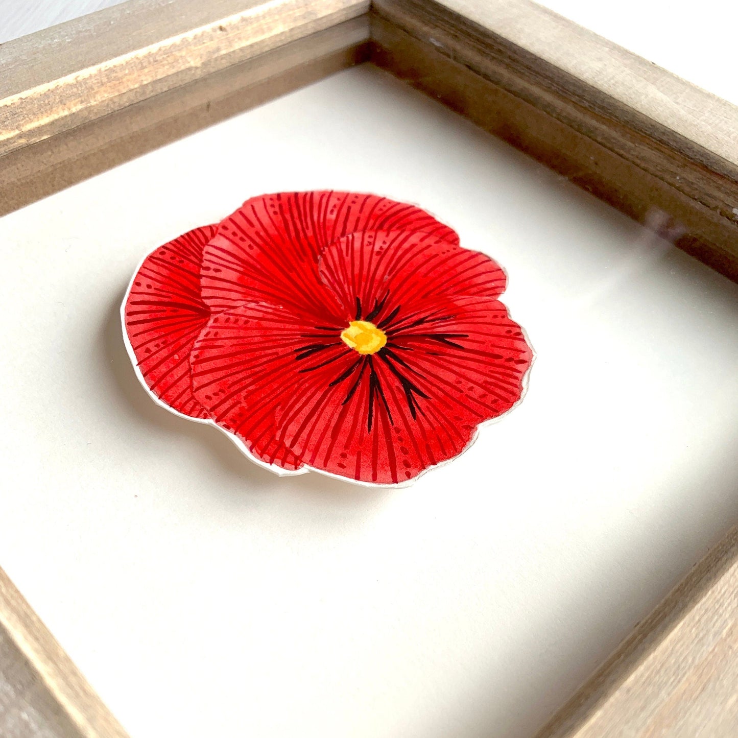 close up of a red pansy flower painting showing the texture of the wood frame and the artwork.