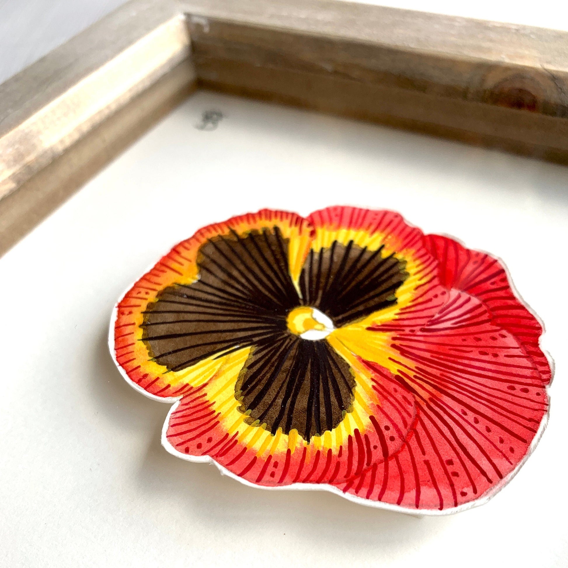 Red yellow and black pansy flower painting in rustic frame showing a close up.