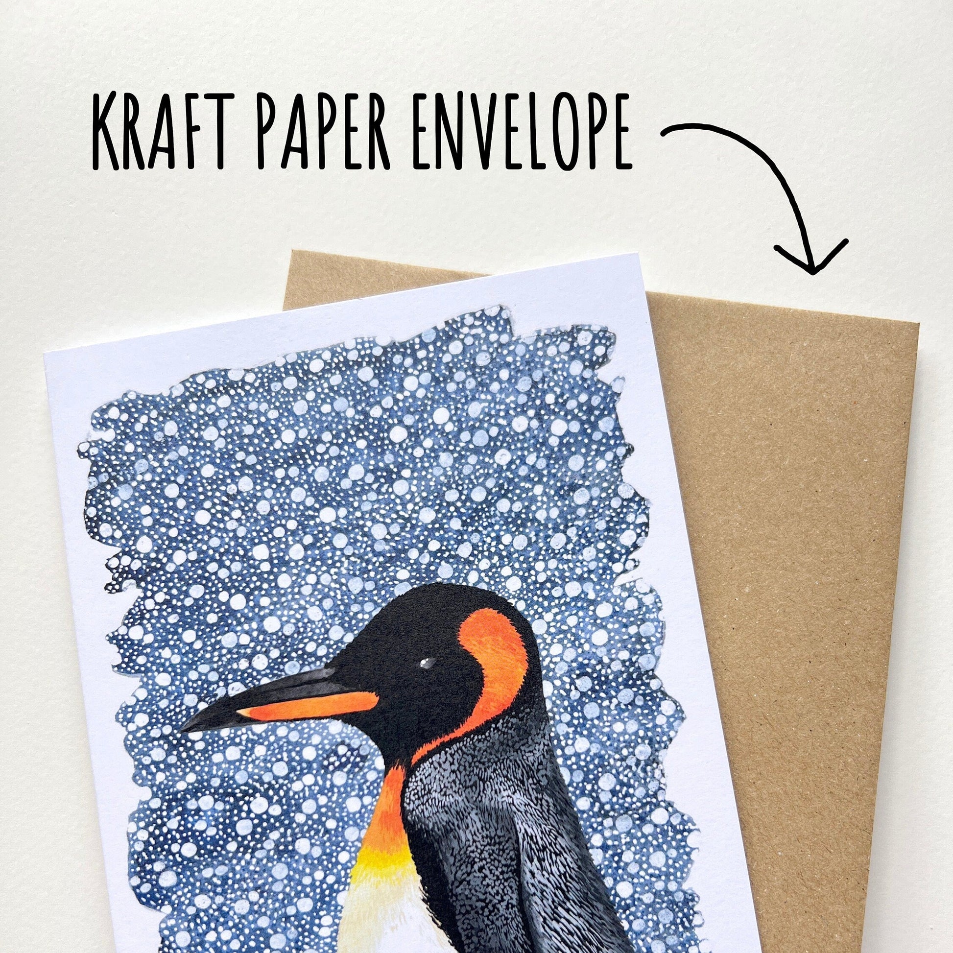 Card with penguin design and 'Merry Christmas' text, held over a kraft paper envelope.